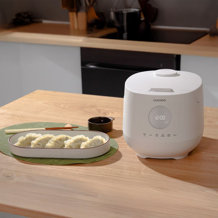 White Cuckoo rice cooker on a kitchen table next to a plate of dumplings and a small bowl of dipping sauce. (CR-0661F)