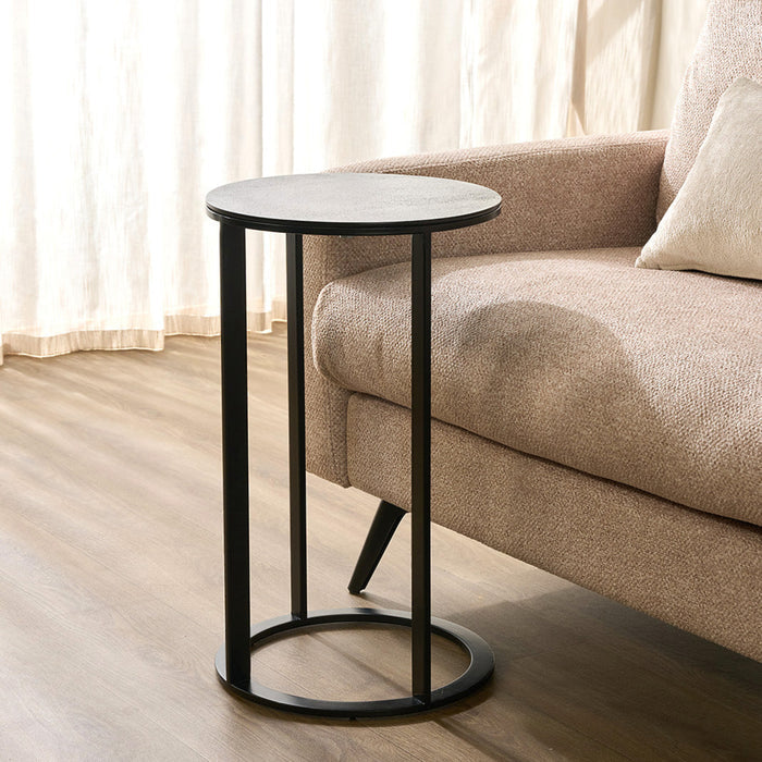 A Callan Marble Side Table in White is a table with a white marble top and slim metal legs, positioned next to a beige sofa on a wood floor in front of sheer curtains.
