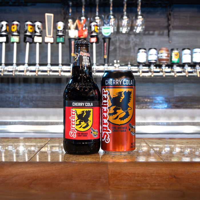 Two bottles of Cherry Cola on a bar counter with beer taps in the background