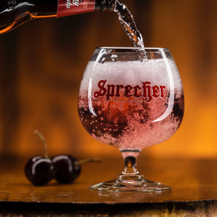 Sprecher Cherry Soda being poured into a glass labeled 'Sprecher' with cherries in the background.