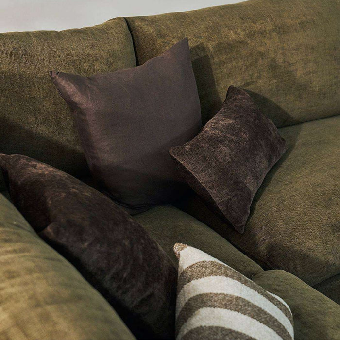 A close-up of a textured olive green sofa with several dark brown throw pillows, including one striped accent pillow in the foreground.