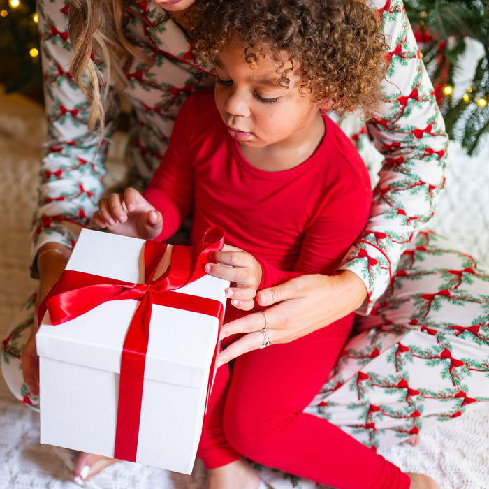 Young toddler sitting on mothers lap wearing the Long Sleeve Pajamas in Cardinal opening a gift