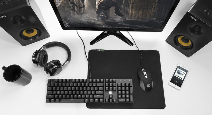 Plugable MP-SCL black polyester micro-weave hybrid surface mouse pad on a desk with keyboard, mouse, and speakers.