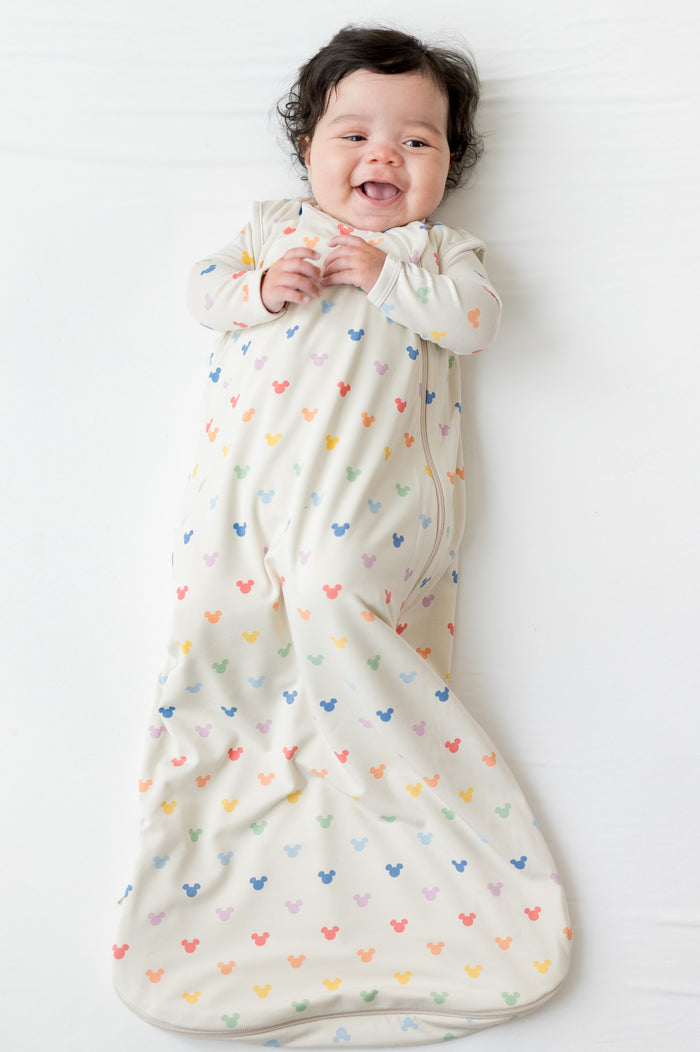 Baby wrapped in a colorful mickey-patterned sleep sack on a white background