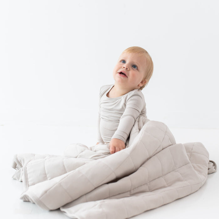 Child sitting while wrapped in a Toddler Blanket in Oat 1.0 TOG