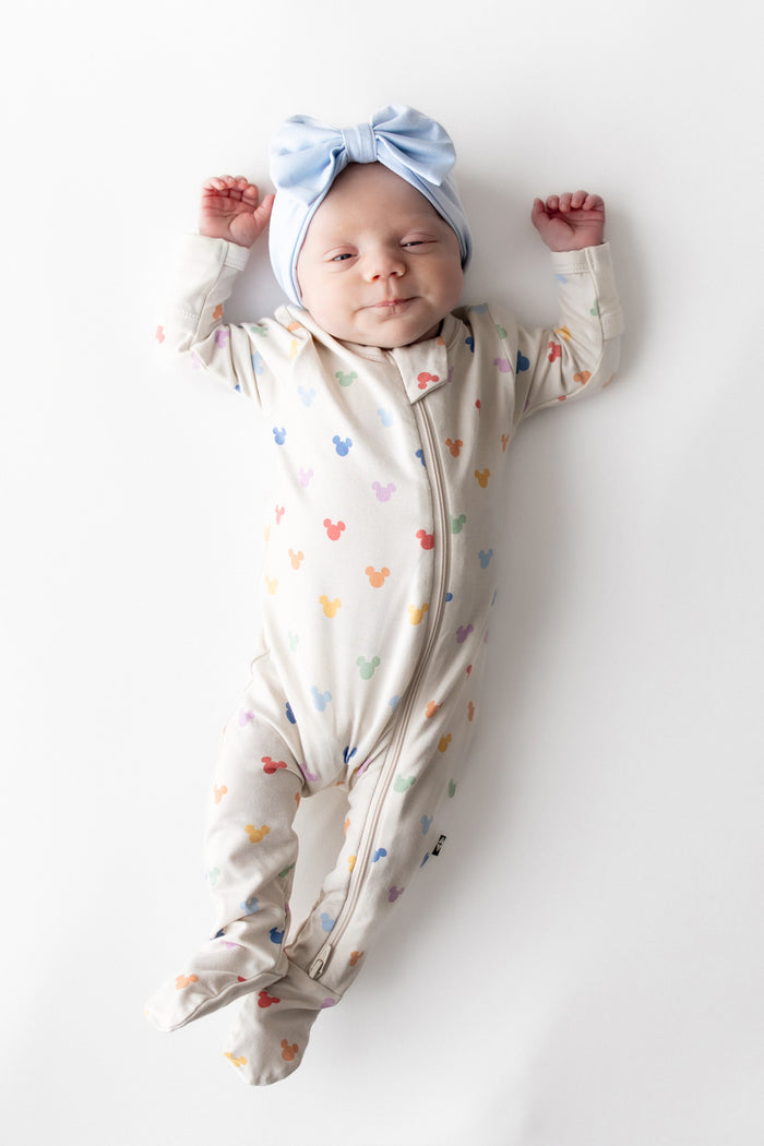 Newborn baby in a colorful mickey footed onesie and blue headband on a white background