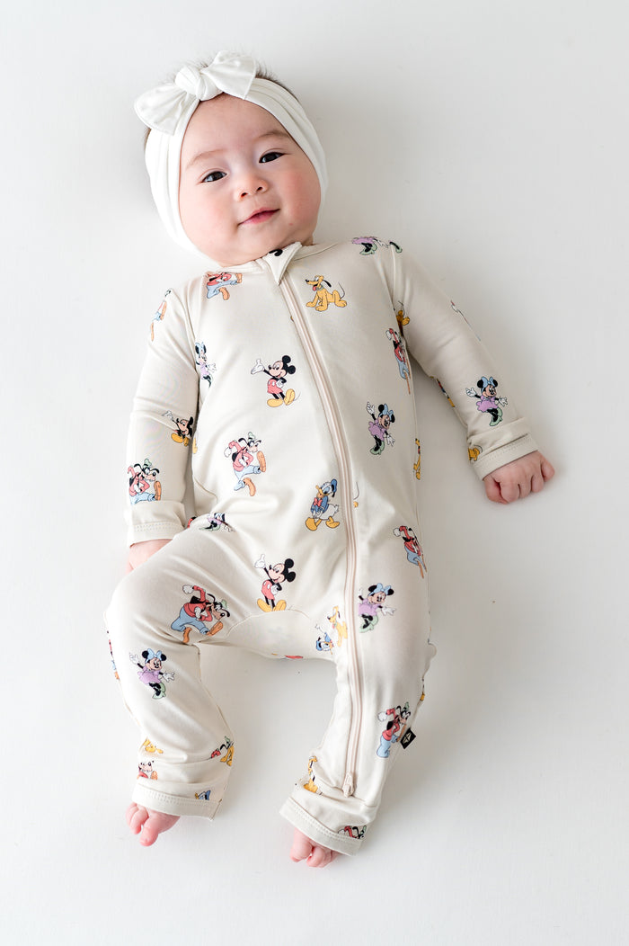 Baby wearing mickey and friends patterned zippered romper and white bow